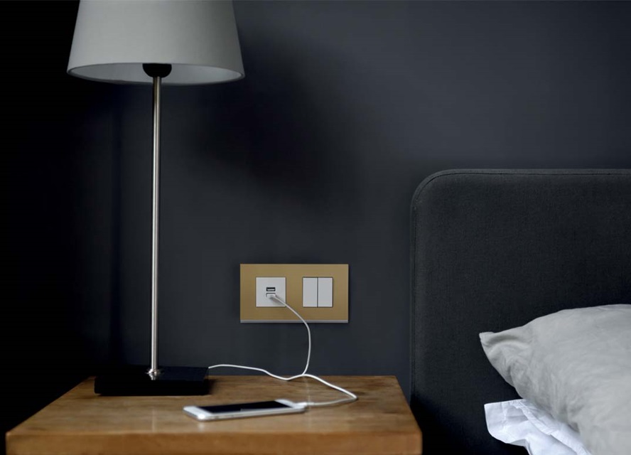 Modern bedroom with a table lamp and wall-mounted electrical switches and socket from Hager