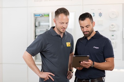 Hager employees discussing over a tablet in front of electrical installation equipment
